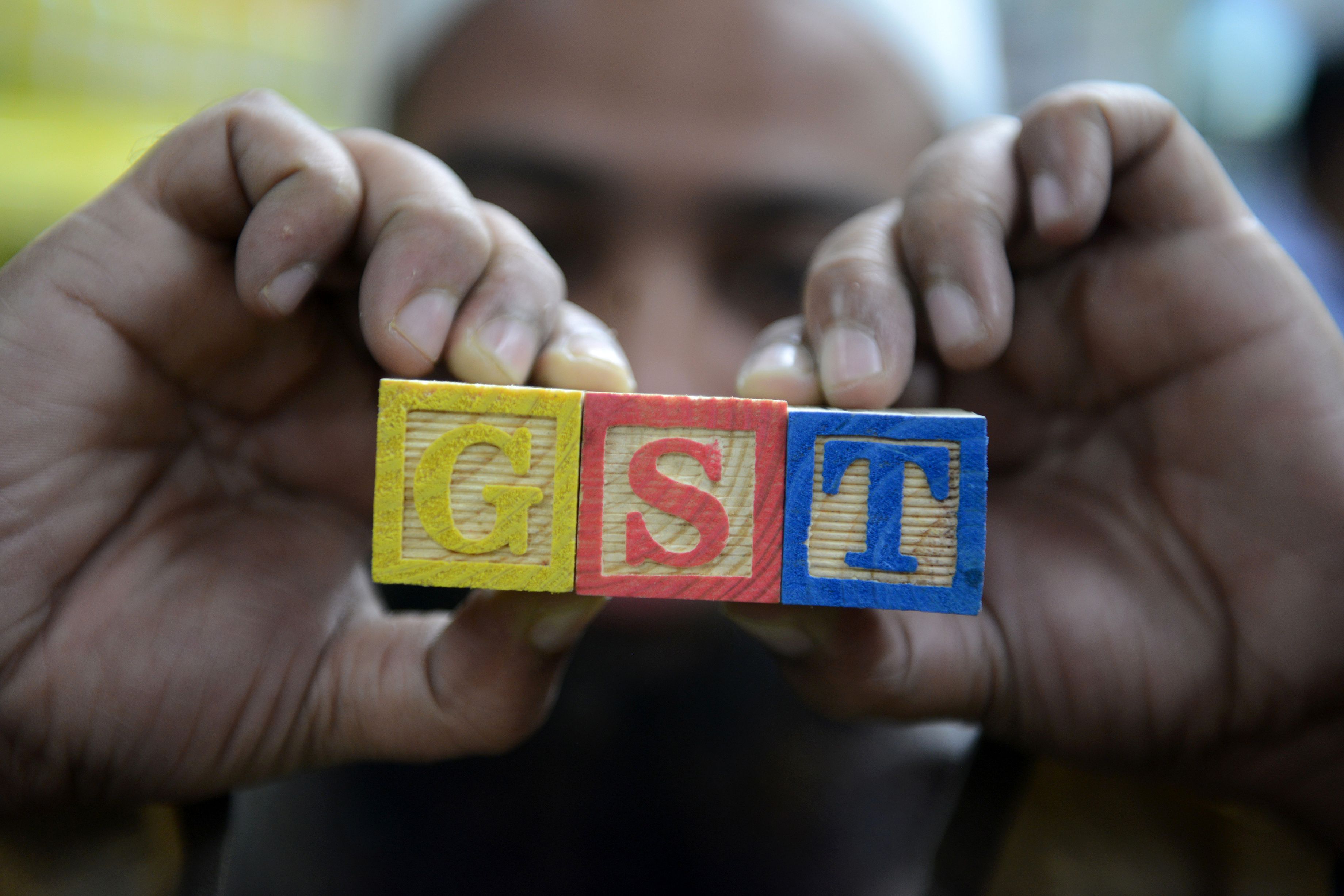 An Indian consumer goods trader shows letters GST representing "Goods and Services Tax" (GST)at his shop in Hyderabad on August 3, 2016. Finance Minister Arun Jaitley said India was on the cusp of its biggest tax reform since independence ahead of a vote in parliament later August 3, on a new national sales tax. The Goods and Services Tax (GST) will replace a patchwork of central and state levies on goods and services and is one of Prime Minister Narendra Modi's biggest reforms since taking power in May 2014 . / AFP PHOTO / NOAH SEELAM